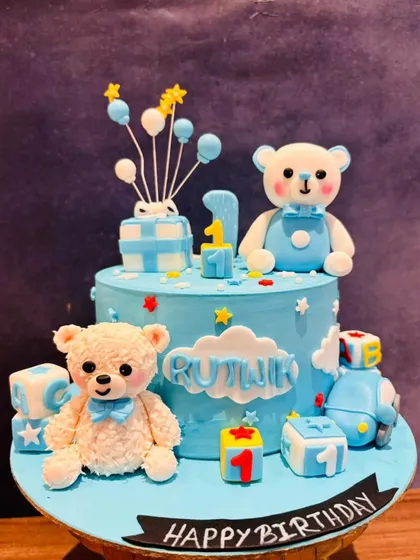 An adorable teddy bear themed cake for a little boy's first birthday. This cute blue cake is decorated with two sweet teddy bears, building blocks, and balloons.