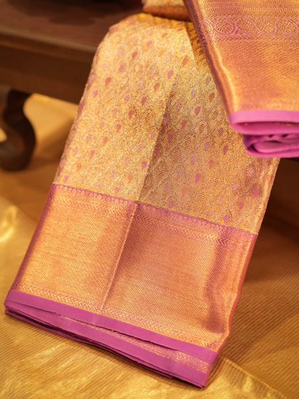 A bridal Kanjivaram in gold and pink brocade, laid out to showcase its rich texture and luxurious feel, perfect for a bride's trousseau.