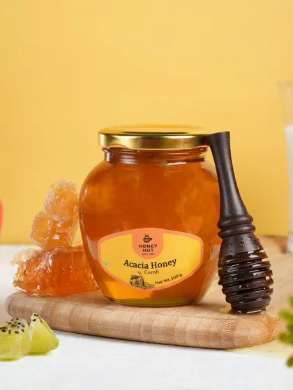A jar of acacia honey with a honeycomb, styled with fresh fruits. This composition highlights the product's natural origins and versatility.