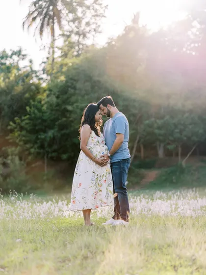 A full-length portrait of the couple standing in a field during golden hour. The soft, warm light and natural surroundings create a romantic and dreamy atmosphere.