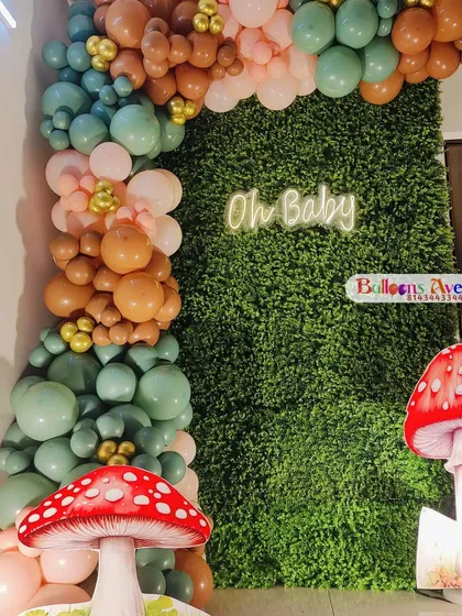 A unique woodland-themed baby shower featuring a lush green grass wall, an 'Oh Baby' neon sign, and mushroom props.