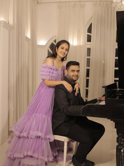 The couple posing with a piano, creating a classic and elegant pre-wedding photo. The lavender gown looks stunning in this setting.