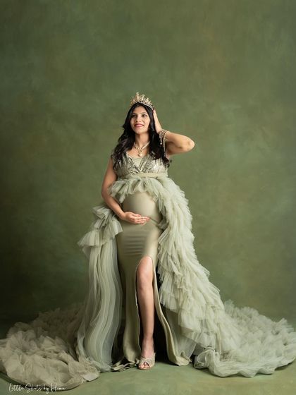 A regal portrait of a queen mother. The expecting mother wears a crown with her stunning olive-green gown, looking up with a powerful and confident expression.