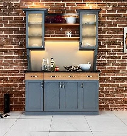 An industrial-style crockery unit with a blue-grey finish set against a brick wall. The frosted glass doors and warm lighting create a chic, rustic look.
