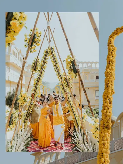 The couple's joyful entrance through a triangular archway decorated with marigolds at their Jaipur Haldi ceremony.