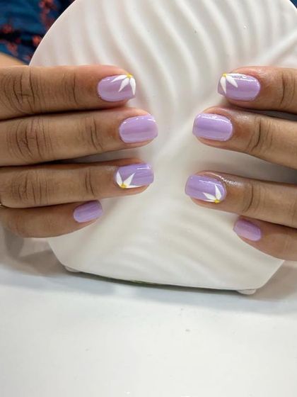 A cute and simple design on short, natural nails. This features a solid lilac base with minimalist white floral petal art on the accent nails.