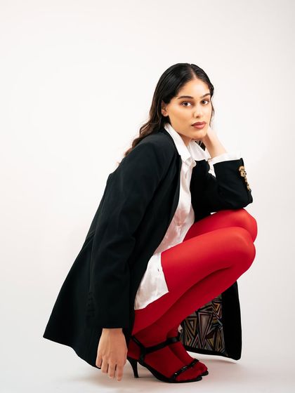 A crouching pose that adds an edge to this power-dressing look. This shot showcases the full outfit, including the detailed lining of the blazer and the heeled shoes.