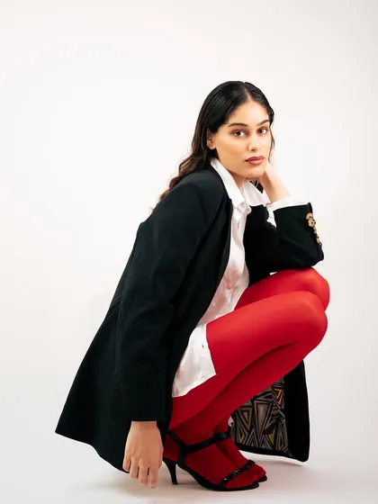 A crouching pose that adds an edge to this power-dressing look. This shot showcases the full outfit, including the detailed lining of the blazer and the heeled shoes.