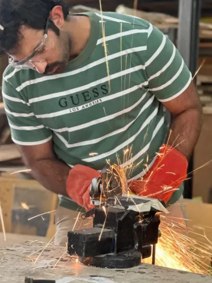 Sparks fly as a maker grinds down a piece of scrap metal. This process is key for cleaning edges and preparing surfaces for welding, ensuring a strong and professional finish.