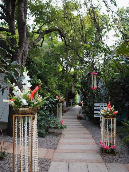 The pathway at Farmhouse Collective is decorated with beautiful floral stands for a Seemantham (baby shower) ceremony, creating an elegant and welcoming entrance for guests.