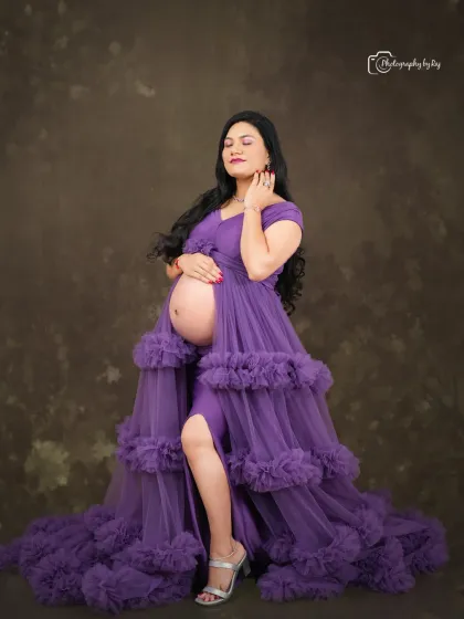 A glamorous studio portrait of a mother-to-be in a purple ruffled gown, showing off her bare bump.