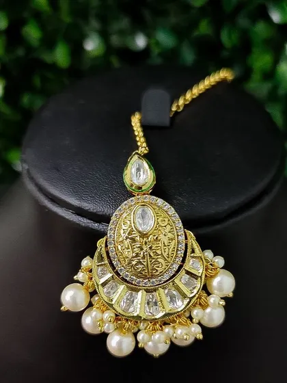 Another elegant chaand bali style maang tikka with a polished gold finish and pearl accents.