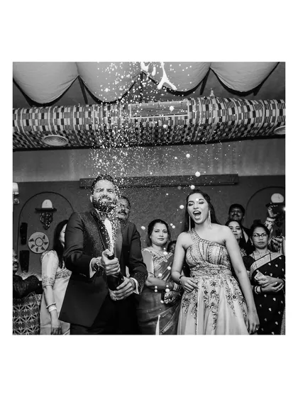 A classic black and white shot of the groom popping a bottle of champagne, with the bride's excited reaction captured perfectly. A moment of pure celebration.