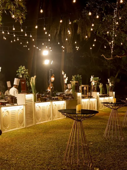 I transform venues into magical spaces. This is an evening reception setup with elegant food counters, ambient lighting, and high top tables, creating a sophisticated and inviting atmosphere for guests to mingle and dine.