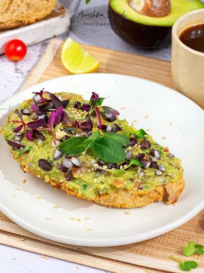 A beautiful shot of avocado toast with a coffee. The natural light and shadows from a palm leaf create a lovely, relaxed, cafe-style atmosphere.