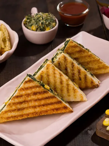 A classic spinach and corn grilled sandwich, sliced to show the delicious filling. We focus on creating clean, appetizing images for cafe menus and online ordering platforms.