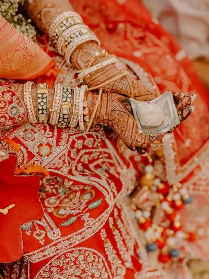 A candid moment from a wedding ceremony, with the bride's mehendi-adorned hands holding a traditional element of the ritual.