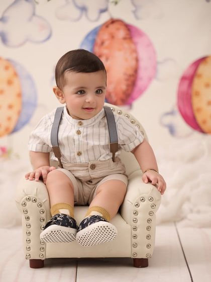 Looking dapper in his mini armchair. This hot air balloon themed backdrop adds a touch of whimsy to a classic sitter portrait.