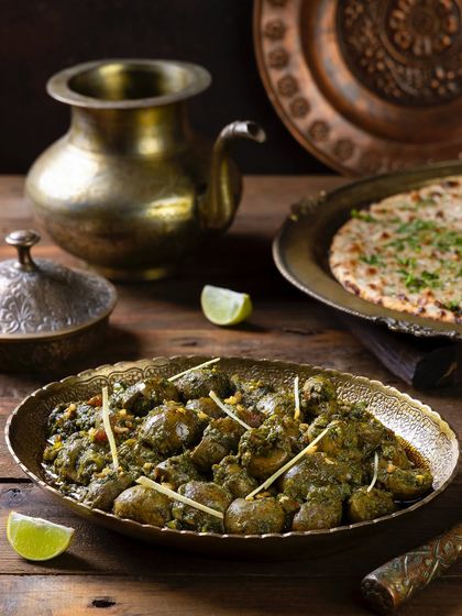 Palak Gurda, a spinach-based curry, presented with naan. The lighting brings out the vibrant green of the spinach gravy.