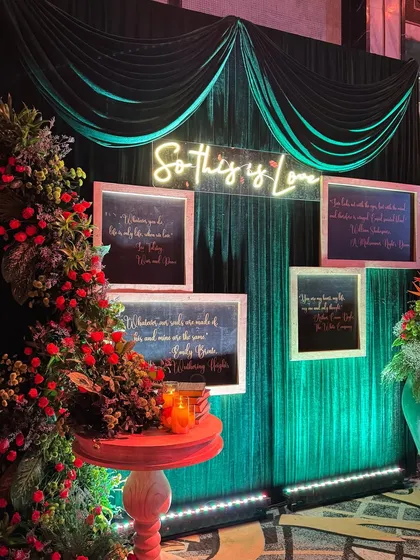 "So This Is Love." A romantic and moody photo-op corner, with a neon sign, framed love quotes, and a backdrop of dark green velvet.