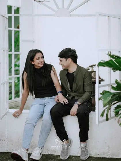 The couple sharing a happy, relaxed moment, seated in a white window frame, a perfect pre-wedding portrait.