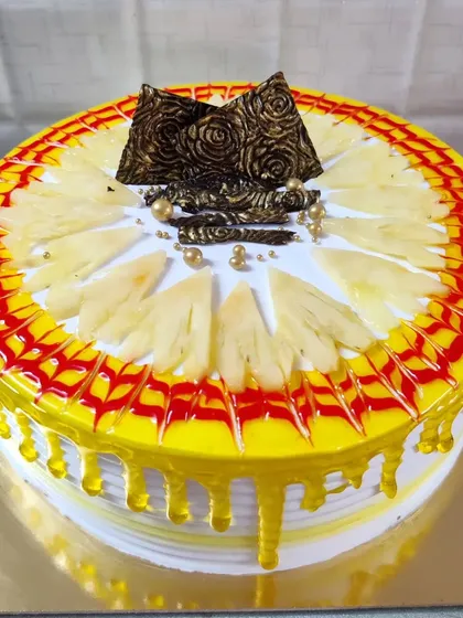 A pineapple cake with a yellow drip glaze. The top is decorated with fresh pineapple slices and chocolate accents.