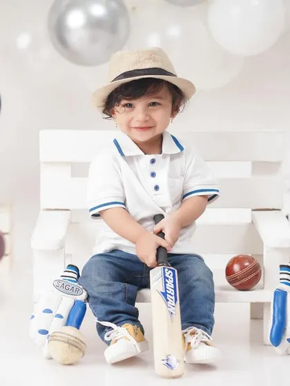 A future cricket star in the making, this little boy is all smiles in a 'Little Cricketer' themed shoot, complete with a bat, balls, and helmet.