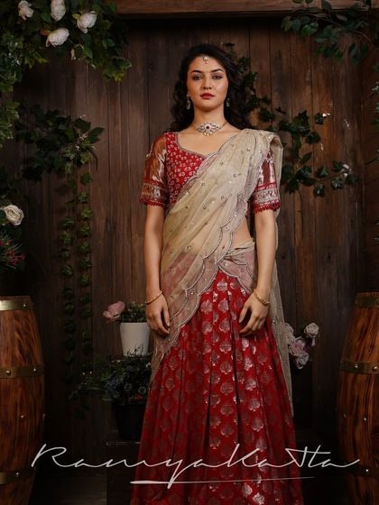 This bright cherry red Benaras lehenga offers a timeless bridal look. Paired with a contrasting rose gold embroidered blouse and a double scalloped tulle dupatta, it is the epitome of grace.