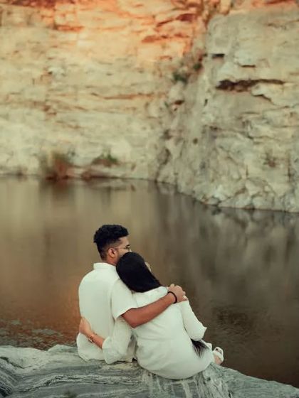 A loving embrace as the couple sits on a rock overlooking a calm lake. This composition emphasizes both the couple's connection and the beautiful scenery.