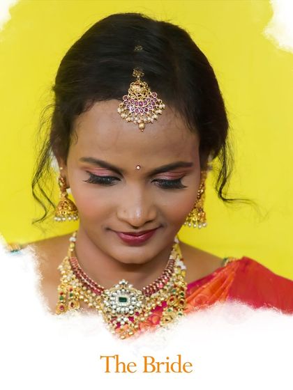 A classic bridal portrait against a simple yellow background. Her downward gaze and soft smile create a serene and graceful image, focusing on her beautiful makeup and temple jewellery.