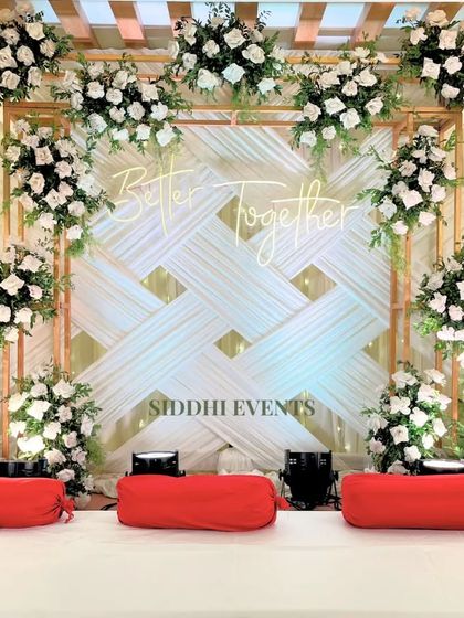 This Sangeet stage features a 'Better Together' neon sign against a woven white backdrop, framed by lush white floral arrangements for a celebratory feel.