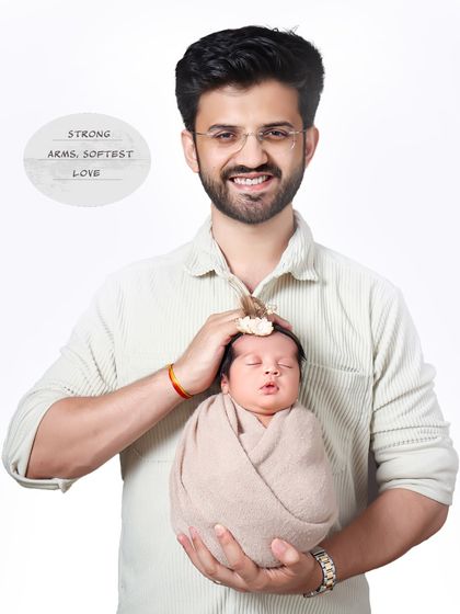 Strong arms, softest love. A proud father smiles at the camera while gently holding his sleeping newborn, a beautiful contrast of strength and tenderness.