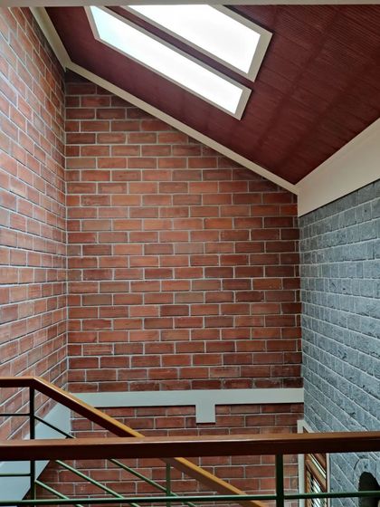 A sloping roof with skylights meets a combination of brick and stone walls, showcasing the junction of different materials and forms.