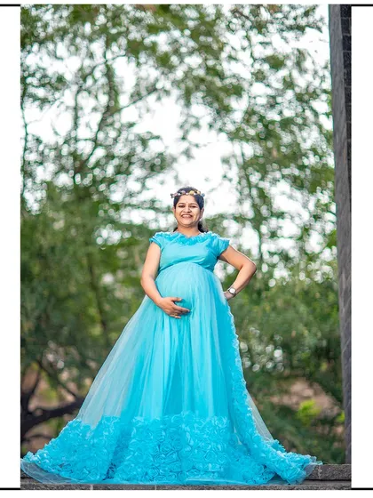 A proud and happy mom-to-be posing in a beautiful light blue gown with a floral-textured train.
