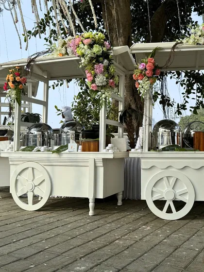Two of our classic white food carts, ready for service at an outdoor event. The floral decor adds a touch of elegance and ties the whole setup together.