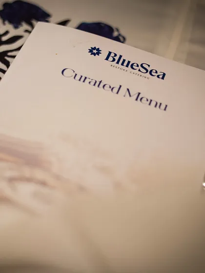 A close up of a "Curated Menu" card, resting on an elegant plate. This simple detail signifies our bespoke approach to every event we host at our venues or cater for externally.