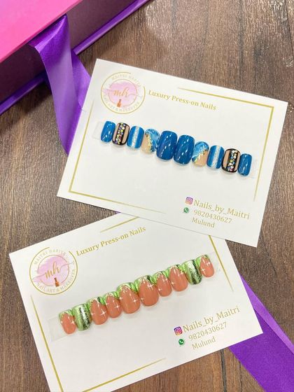 Two different custom press-on sets ready to be shipped. One features a bold blue design with rhinestone accents, while the other has a more earthy green and brown palette.