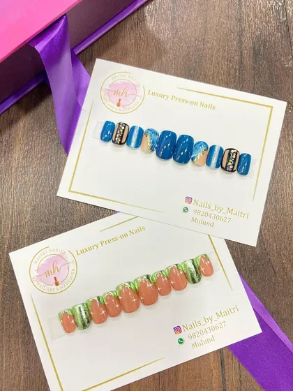 Two different custom press-on sets ready to be shipped. One features a bold blue design with rhinestone accents, while the other has a more earthy green and brown palette.