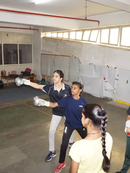 A senior fencer demonstrates the correct form to younger students. We foster a culture where experienced athletes help guide the next generation.
