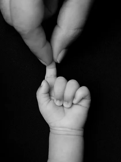 A parent's finger held by a newborn's tiny hand. This black and white photo is a simple, iconic, and deeply emotional image of the parent-child bond.