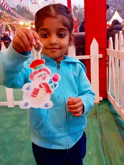 A proud young artist holding up her snowman ornament, created during our parchment craft workshop at a festive flea market.