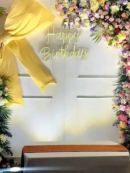 A beautiful 'Happy Birthday' photo backdrop, framed with a profusion of pastel flowers and a large yellow fabric bow.