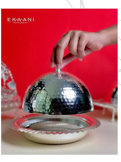 A hand lifts the hammered cloche, revealing the dish below. It is a perfect blend of style and function, creating a moment of drama at the dinner table.