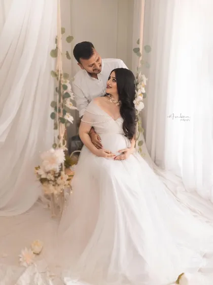 A romantic couple's portrait on the white-themed swing set. Their loving gaze and the dreamy, ethereal setup make for a perfect, fairytale-like maternity photo.