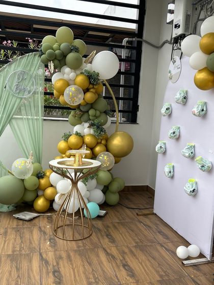 A modern and fresh baby shower decor setup on a balcony. This design uses a ring backdrop with a balloon garland in shades of green, yellow, and white.