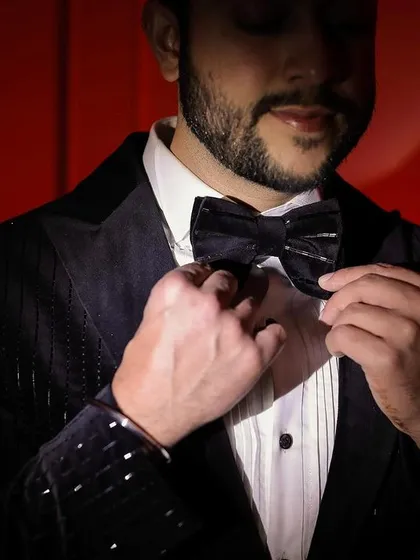 A close-up of the groom adjusting his bow tie, with a dramatic red background creating a bold and stylish look.