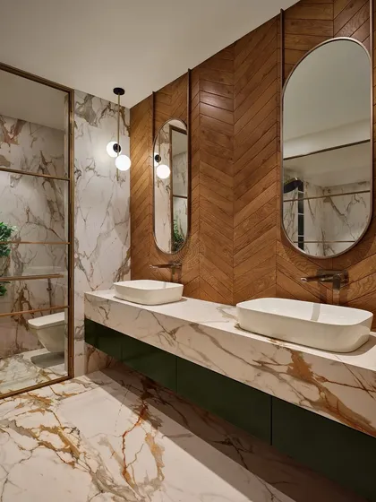A luxurious master bathroom featuring a mix of materials. The walls combine herringbone wood paneling with dramatic, gold-veined marble, which is also used for the double vanity countertop.