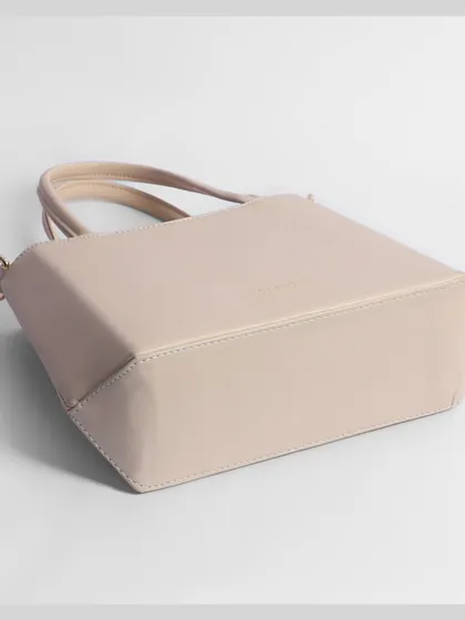 The base of a beige handbag, shot at an angle to highlight its structure and shape.