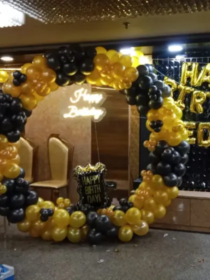 A stylish black and yellow balloon ring setup in a banquet hall. This design includes a 'Happy Birthday' neon sign and a black sequin wall with foil letters spelling out the name.