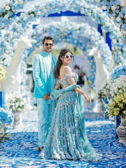 The couple walks down a path adorned with blue and white floral arches, creating a dreamy and picturesque setting for their royal wedding.